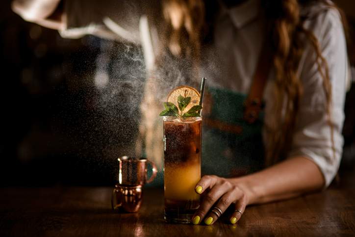 Close-up of glass with coffee cocktail and female bartender gently sprinkles on it